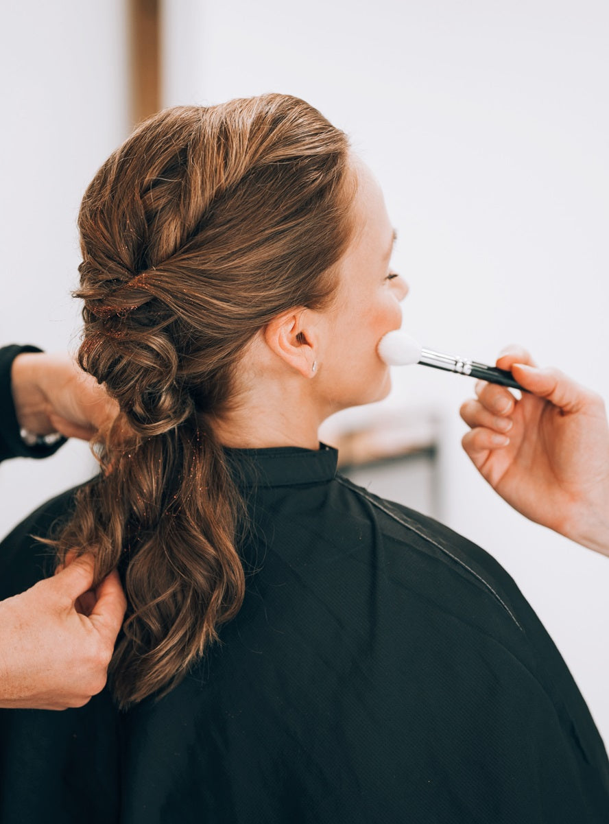 Zwei Personen erstellen eine Hochsteckfrisur und Makup bei einer Kundin