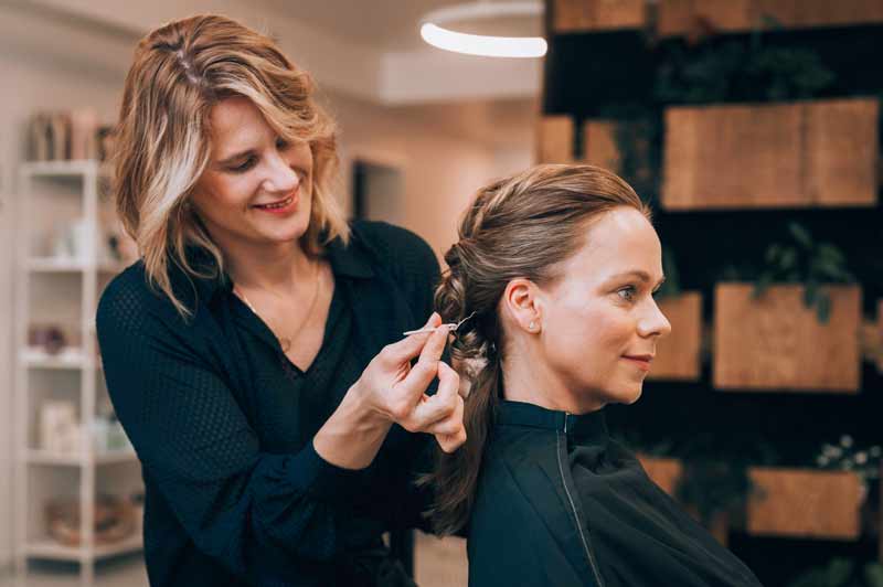 Die Friseurin steckt einer Kundin die Haare zu einem Zopf.
